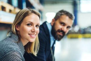 A portrait of an industrial man and woman engineer in a factory, looking at camera.